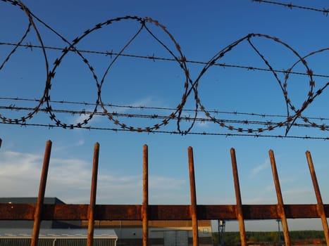Barbed wire in skeins and stretched against the blue sky. Barbed wire against thieves and vandals. An insurmountable obstacle. Rusty wire, rows, spiral and coils of barbed wire