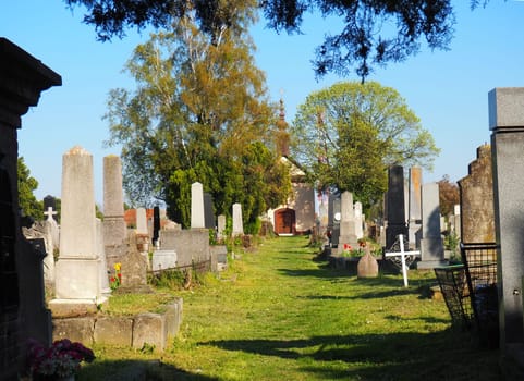 Sremska Mitrovica, Serbia, April 26, 2021. Catholic cemetery with graves, monuments, pedestals, columns and granite slabs. The road in the center of burial. Chapel in the distance.