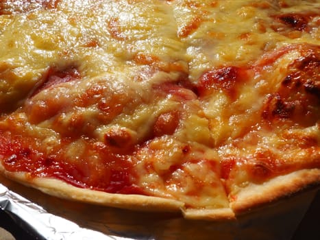 Pizza with tomatoes and cheese in a cardboard box and aluminum foil. Delicious pizza close up. Courier delivery of food to your home. Ordering pizza. Traditional Italian round yeast cake with filling.