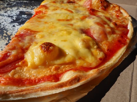 Pizza with tomatoes and cheese in a cardboard box and aluminum foil. Delicious pizza close up. Courier delivery of food to your home. Ordering pizza. Traditional Italian round yeast cake with filling.