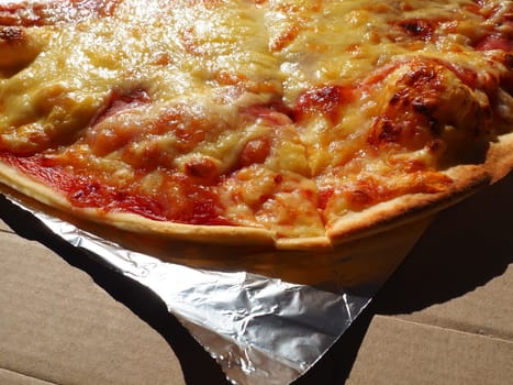 Pizza with tomatoes and cheese in a cardboard box and aluminum foil. Delicious pizza close up. Courier delivery of food to your home. Ordering pizza. Traditional Italian round yeast cake with filling.