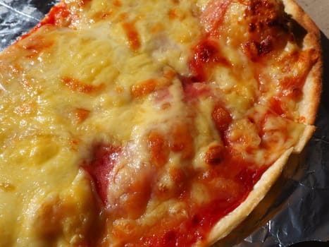 Pizza with tomatoes and cheese in a cardboard box and aluminum foil. Delicious pizza close up. Courier delivery of food to your home. Ordering pizza. Traditional Italian round yeast cake with filling.