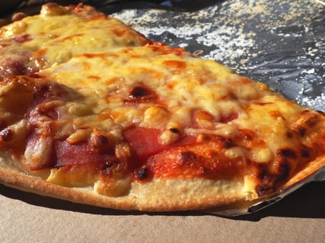 Pizza with tomatoes and cheese in a cardboard box and aluminum foil. Delicious pizza close up. Courier delivery of food to your home. Ordering pizza. Traditional Italian round yeast cake with filling.