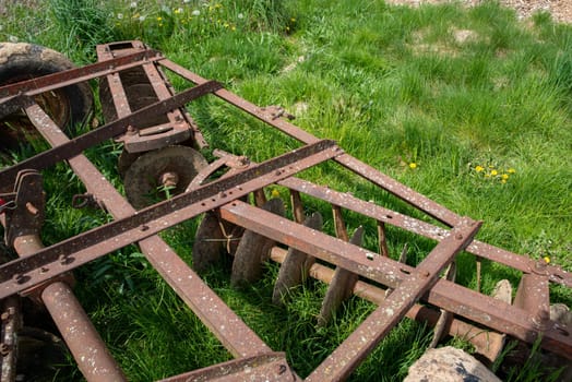 Old metal harrow in a green grass field with dandelions in the bright sunshine. Rows of muddy discs are visible on vintage traditional equipment. copy pace and no people.