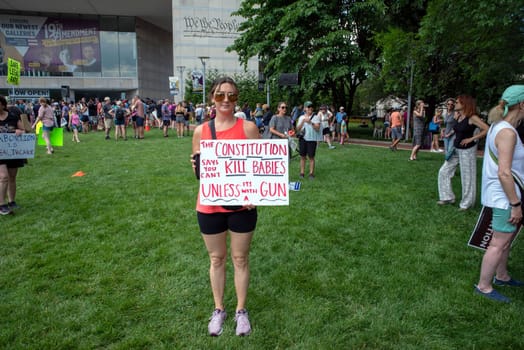 Philadelphia, PA USA 06/25/2022 Woman at a political pro-choice rally holds a sign that reads THE CONSTITUTION SAYS YOU CAN'T KILL BABIES UNLESS IT'S WITH A GUN. Large gathering crowd behind her.