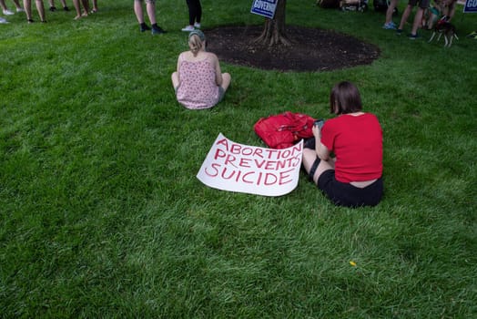 Philadelphia, PA USA - 06-25-2002 Woman at a political pro-choice rally sits in the grass next to  a feminist sign that reads ABORTION PREVENTS SUICIDE as other demonstrators gather. Josh Shapiro rally. Editorial use only.
