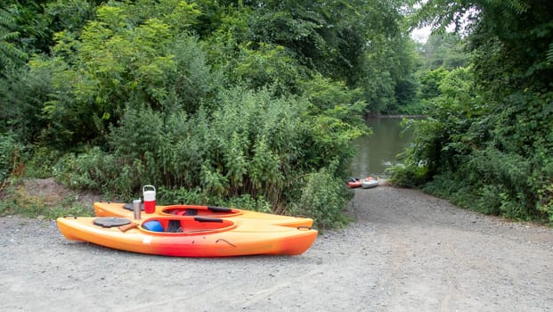 Beautifu l green lush foliage on trees surrounding a river with a path to the water through the trees and two kataks and equipment on the ground. Summer adventure concept family vacation.