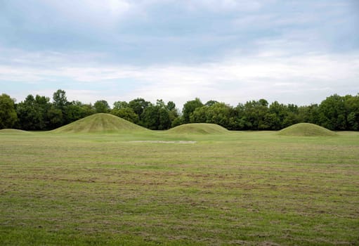 Native American Hopewell Culture prehistoric Earthworks burial mounds in Mound City park Ohio. Ancient circular mounds and long mounds in a row. Grass is neatly trimmed with trees and dramatic sky.