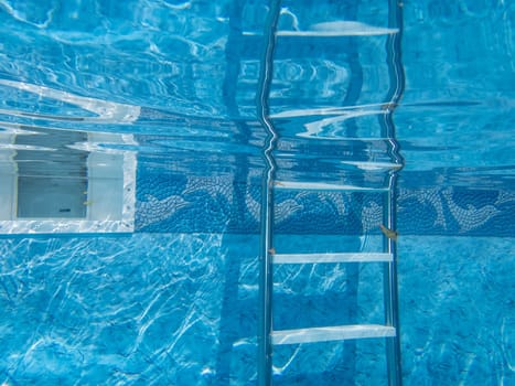Beautiful clean blue water and decorative pool liner with ladder and skimmer pool equipment underwater camera captures tranquil scene with reflection. Copy space, no people, shot outdoors in natural light.