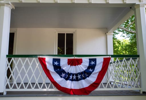 A round American flag Fourth of July decoration hangs on a the front porch of a colonial Pennsylvania house with architectural features and tall windows. No people with copy space.