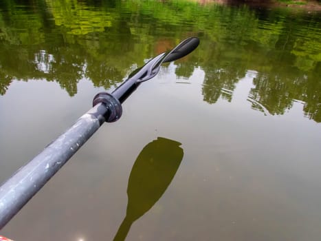 Adventure river scene with raised paddle oar and smooth watr surface with woodland riverbank reflected