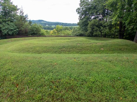 Side view closeup of the coiled tail of the snake at Serpent Mound in Ohio, the largest effigy mound in the world. Ridges of the prehistoric Native American engineering earthwork art are clearly visible covered in green grass with trees and dramatic sky background and no people.