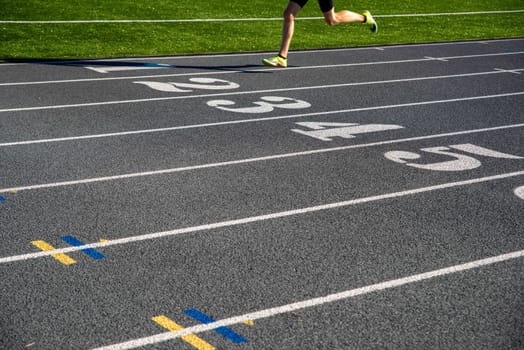 A runner on a gray athletic running track with large white numbers. Runner races over numbers with copy space. Selective focus on track for excellent track and field background.