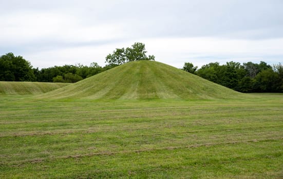 Native American Hopewell Culture prehistoric Earthworks burial mounds in Mound City Ohio. Ancient circular mound in foreground and long mound in the background. Grass is neatly trimmed with trees and dramatic sky.