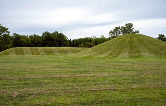 Mound City ancient Hopewell Culture burial mounds, one circular and one long covered in neatly trimmed grass under a dramatic sky