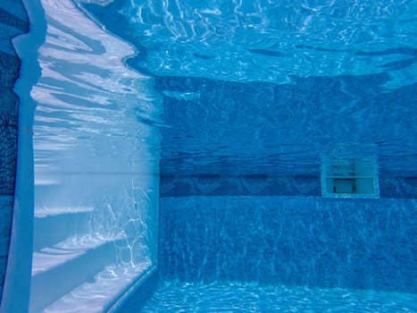 Serene relaxing view of pool steps and dappled light rippling on walls and floor, Blue design on walls taken with an underwater camera. Underside of water surface relects pool bottom.