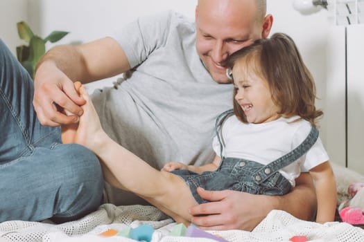 Father plays with little daughter 2-4 on floor. Dad tickles kids feet. Family, having fun