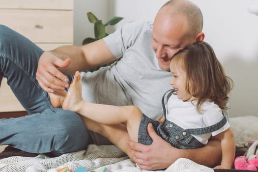 Father plays with little daughter 2-4 on floor. Dad tickles kids feet. Family, having fun