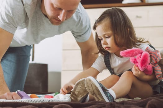 Dad and little girl 2-4 play with constructor and soft toys, sitting on floor at home