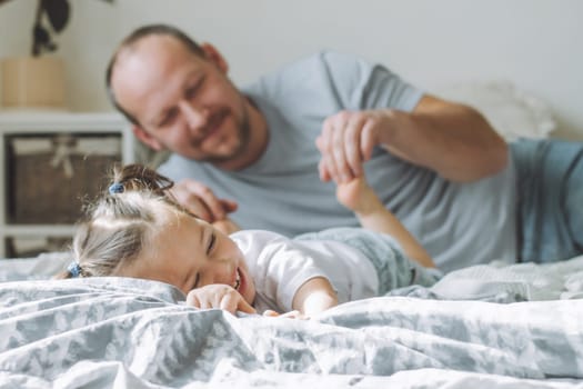 Father plays with little daughter 2-4 on bed. Dad tickles kids feet. Family having fun
