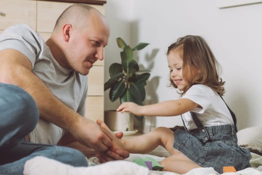 Father plays with little daughter 2-4 on floor. Dad tickles kids feet. Family, having fun