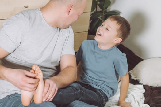 Father plays with his son 7-10 sitting on floor. Dad tickles kids feet. Family having fun