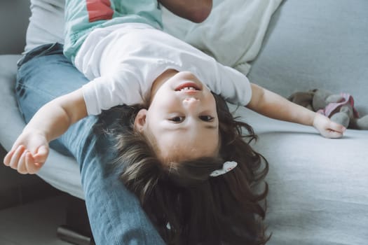 Dad and little girl 2-4 play on the couch. Kid lies on father's lap with her head down and laughs