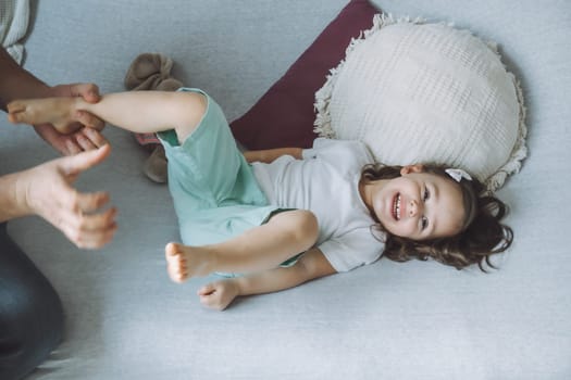 Father plays with little daughter 2-4 on couch. Dad tickles kids feet. Family having fun