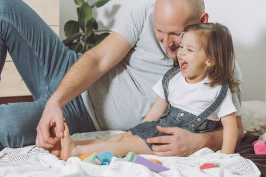 Father plays with little daughter 2-4 on floor. Dad tickles kids feet. Family, having fun