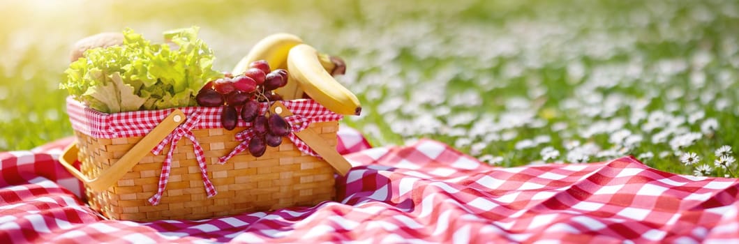 Wicker basket with food standing on the picnic blanket in nature. Concept of the family weekend and romantic picnic.