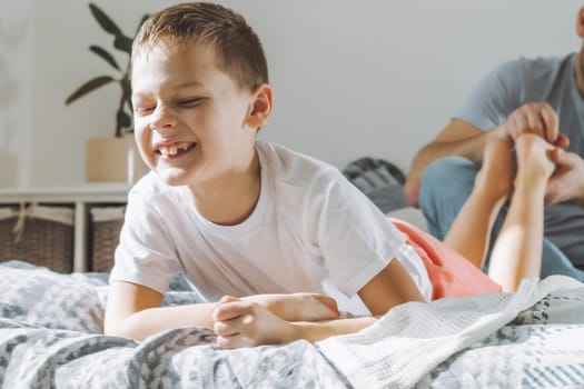 Father plays with his son 7-10 on bed. Dad tickles kids feet. Family having fun