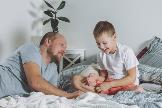 Father plays with his son 7-10 on bed. Dad look at kid and smile. Boy laughing. Family having fun
