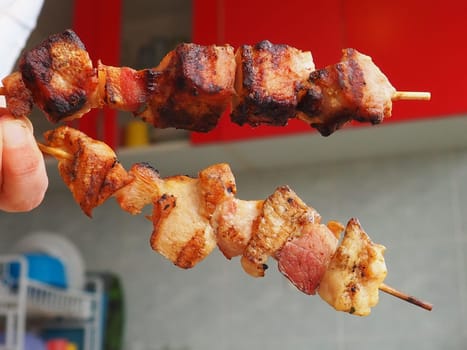 The grilled meat was delivered from the restaurant. Home delivery from restaurants and cafes. Female hands hold meat on a stick. Kitchen with red furniture.