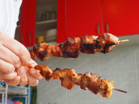 The grilled meat was delivered from the restaurant. Home delivery from restaurants. Women's hands hold meat on a stick. Kitchen with red furniture. Cleanliness and safety of food.