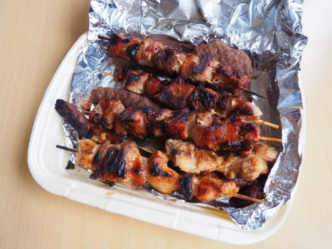 Grilled meat in disposable packaging and aluminum foil, delivered from a restaurant. Food delivery home from restaurants and cafes. Shish kebab and lumpy meat of chicken, pork and lamb.