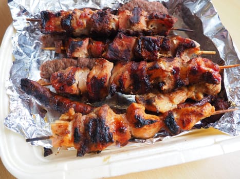 Grilled meat in disposable packaging and aluminum foil, delivered from a restaurant. Food delivery home from restaurants and cafes. Shish kebab and lumpy meat of chicken, pork and lamb.