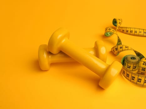 Yellow dumbbells with a tape measure on a yellow background, space for your text, fitness or diet concept
