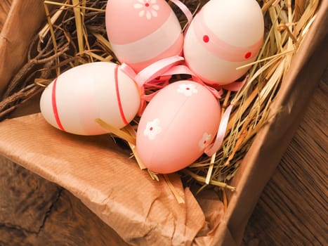 Pink Easter eggs in a cardboard box on a rustic wooden table background with space for text