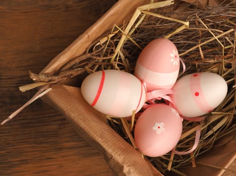 Pink Easter eggs in a cardboard box on a rustic wooden table background with space for text