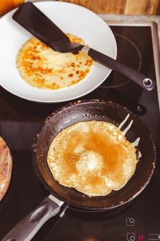 Making thin pancakes on frying pan in kitchen, with cooking dough for crepes and pancakes.