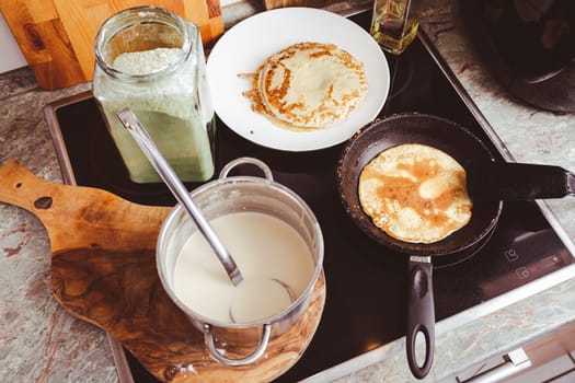 Making thin pancakes on frying pan in kitchen, with cooking dough for crepes and pancakes.