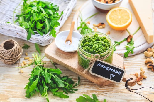 Homemade arugula pesto with ingredients on wooden background