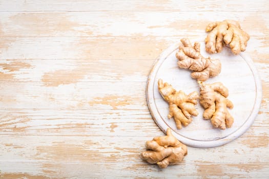 Ginger roots on white wooden background.