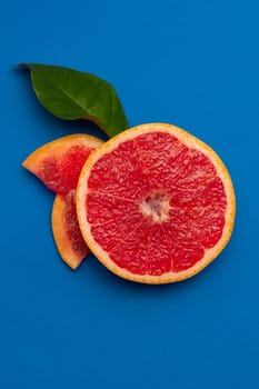 Sliced sides of a grapefruit, three pieces with a green leaf, red pulp isolated on a blue background, vertical shot