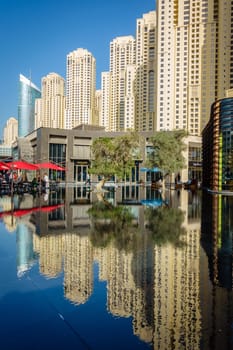 Dubai, UAE, February 23, 2018: Jumeirah Beach Residence (JBR) highrise apartment buildings reflected in a pons at a popular shopping and entertainment area.