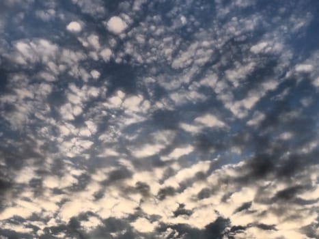 Clouds in the evening sky. The sun's rays pierce the clouds. Blue, yellow and orange colors of the sky and clouds. Beautiful landscape. The sun goes down.