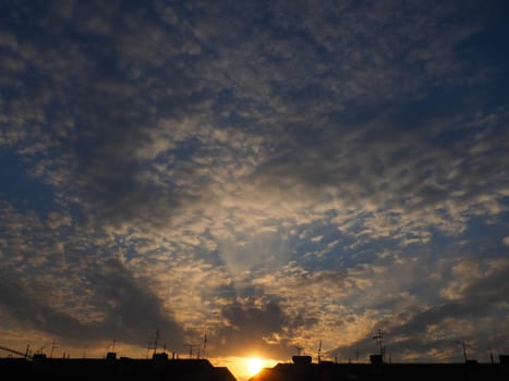 Clouds in the evening sky. The sun's rays pierce the clouds. Blue, yellow and orange colors of the sky and clouds. Beautiful landscape. The sun goes down.