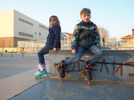 Sremska Mitrovica, Serbia, March 7, 2021. Boy and girl on roller skates on the sports ground. Teenage boy and girl having a rest after roller-skating. Children in demi-season clothes