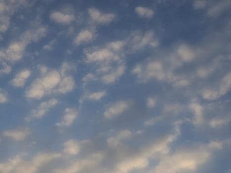 Clouds in the evening sky. The sun's rays pierce the clouds. Blue, yellow and orange colors of the sky and clouds. Beautiful landscape. The sun goes down.