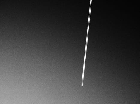 The trail from a flying plane in the sky. Black and white monochrome photography. Kerosene emissions or from heptyl rocket fuel. An ecological concept. Aviation business and passenger transportation.